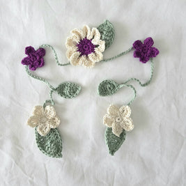 Handmade crochet flower appliqués in cream, purple, and green on white fabric background
