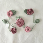 Handmade crochet flower garland with pink blooms and green leaves, perfect for cozy home decor or gifts.