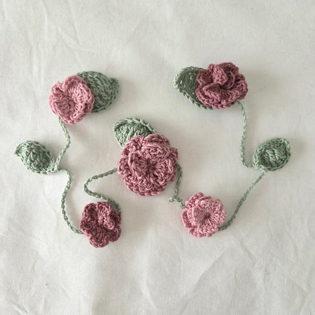 Handmade crochet flower garland with pink blossoms and green leaves on white background