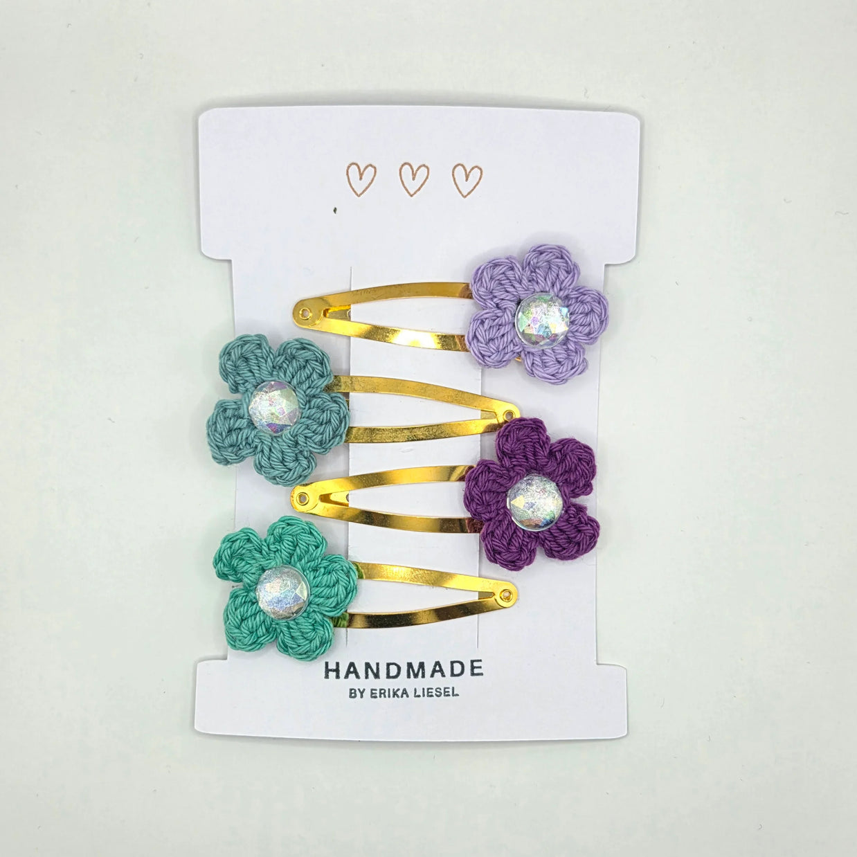 Handmade gold hair clips with crochet flower designs by Erika Liesel on white card.