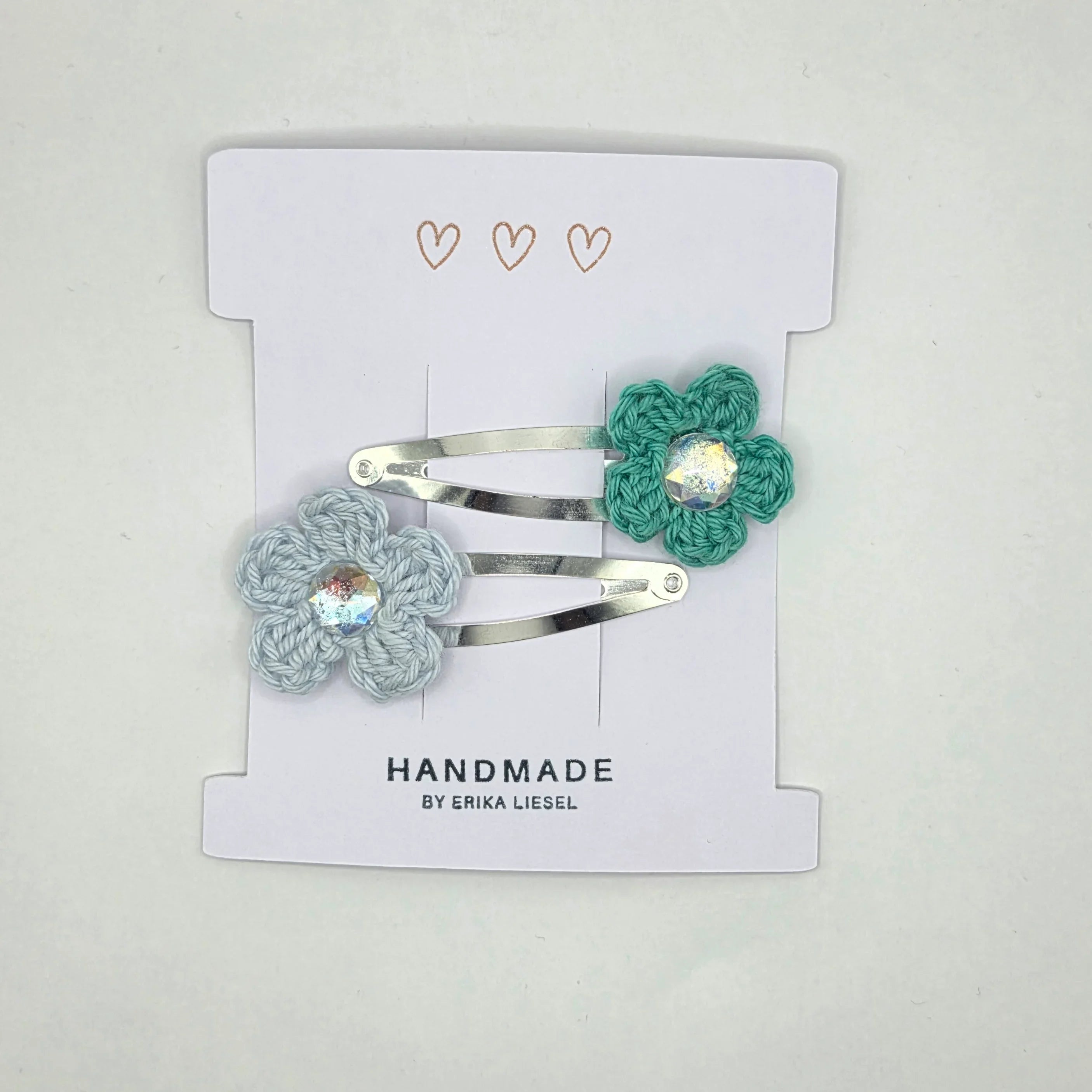 Handmade crochet flower hair clips by Erika Liesel on white card with heart accents