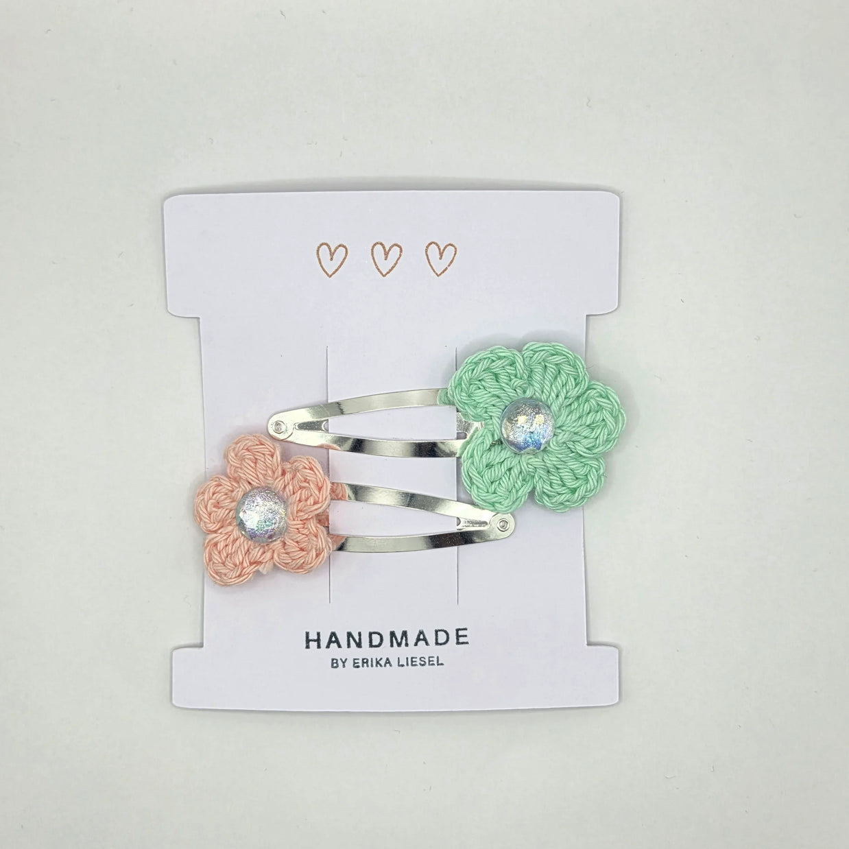Handmade crochet flower hair clips in pastel pink and mint by Erika Liesel on display card