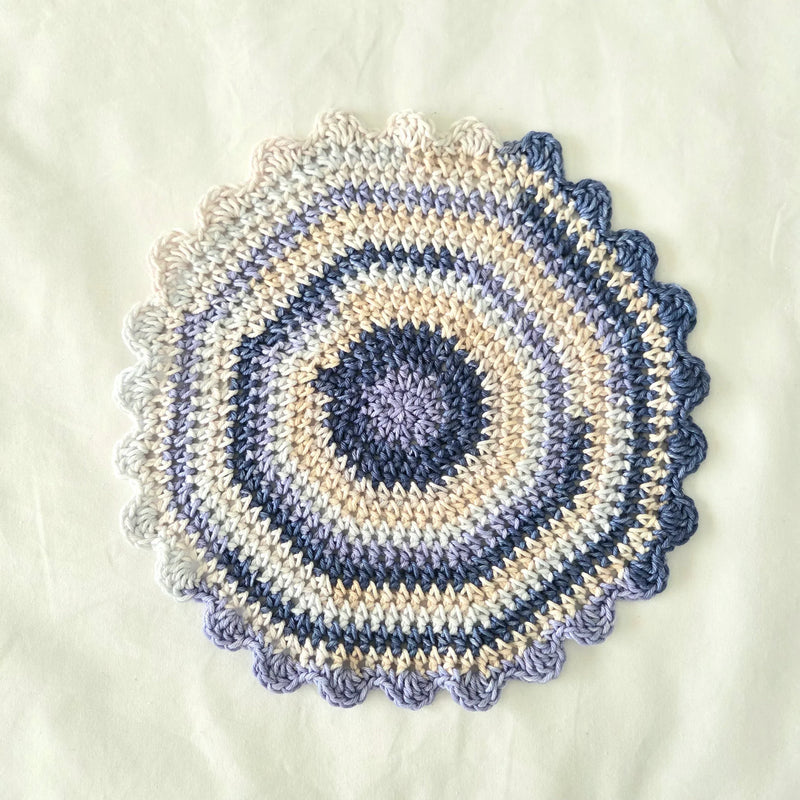 Handmade crochet doily in blue, beige, and lavender with scalloped edge, perfect for cozy home decor.