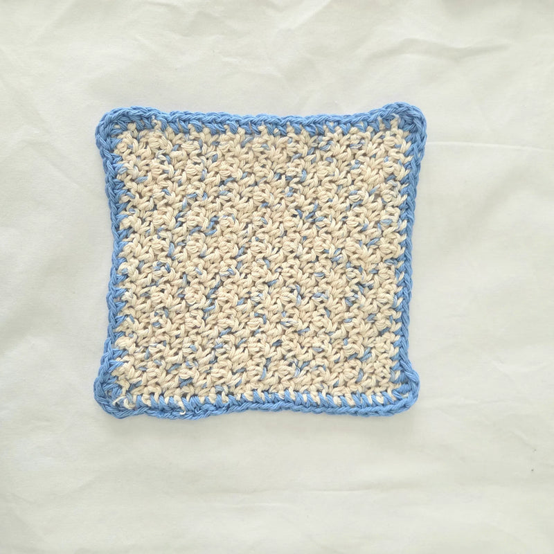Handmade crochet dishcloth with blue border and cream center, cozy kitchen accessory