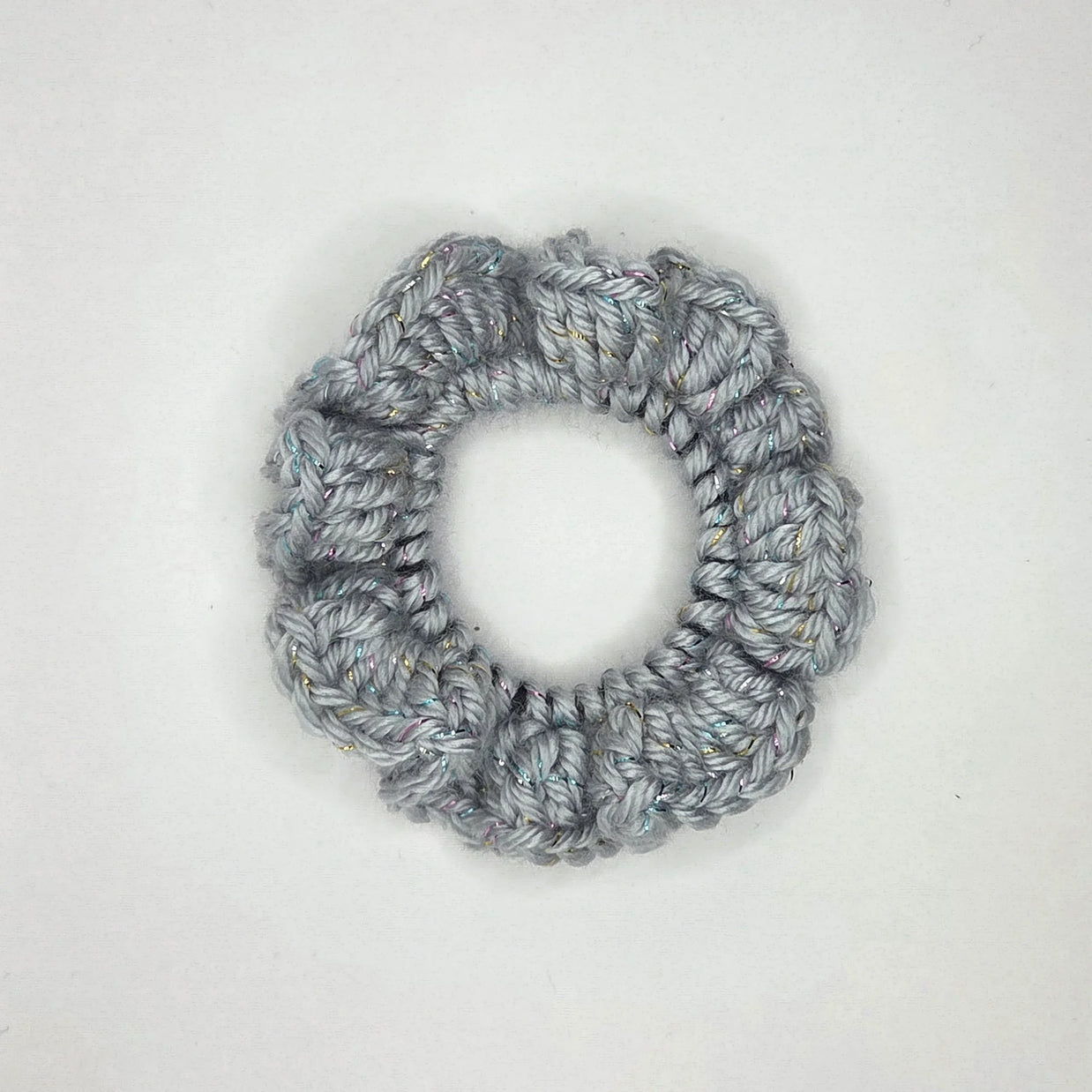 Handmade silver crochet scrunchie with subtle sparkles on a white background