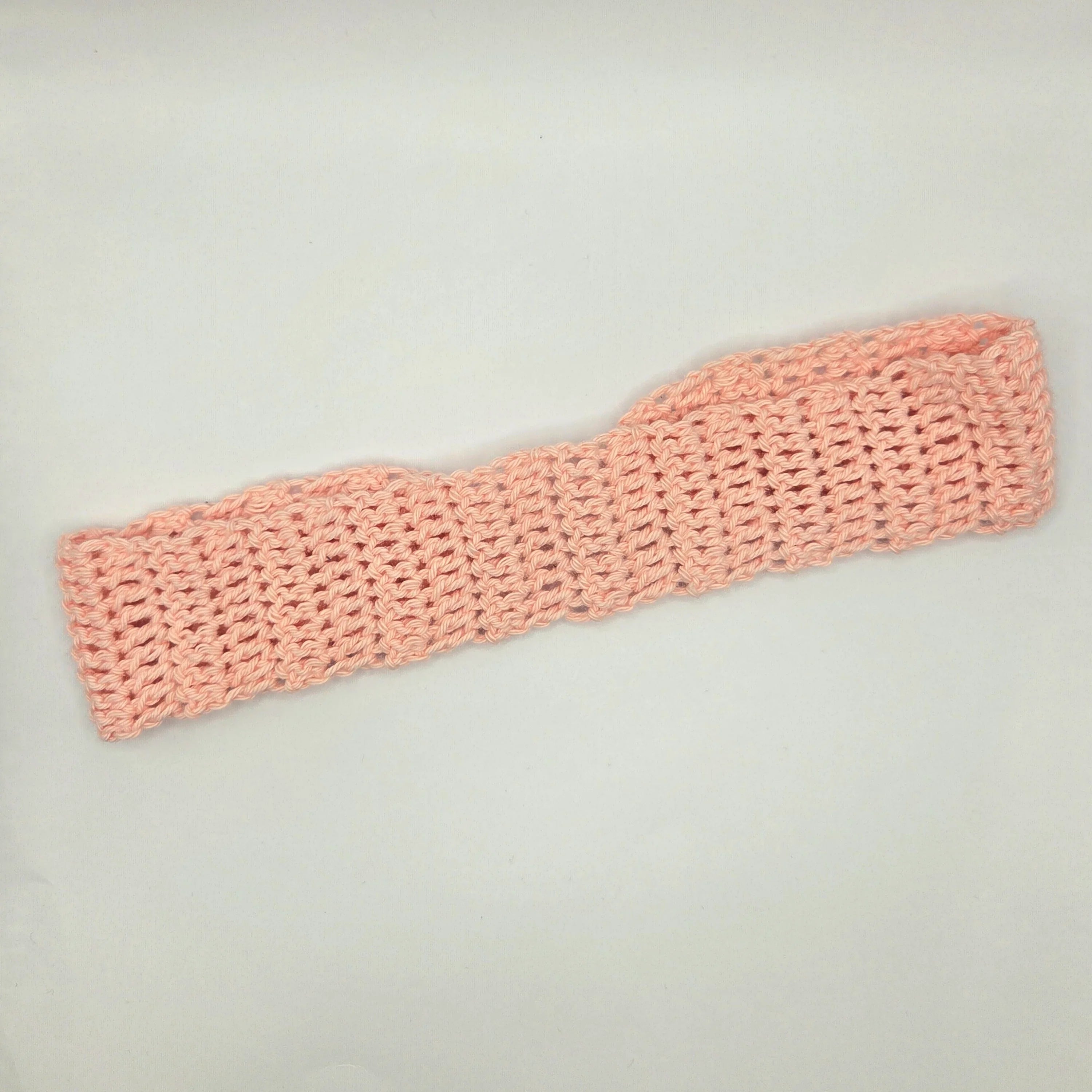 Handmade light pink crochet headband on plain background, cozy gift by Erika Liesel
