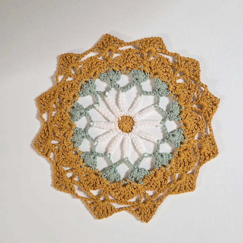 Handmade crochet doily with sunflower design in mustard, sage, and white yarn, perfect for cozy home decor.