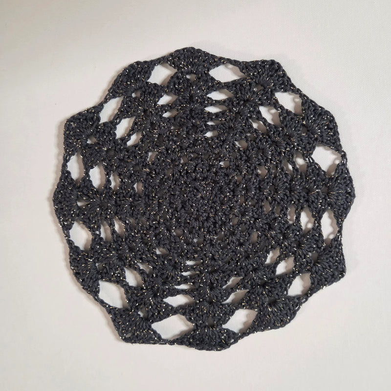 Handmade crochet doily in dark gray with gold flecks, featuring intricate lace pattern and scalloped edges.