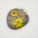 Handmade pressed flower art on smooth gray stone with yellow blooms and twine accent, cozy nature decor