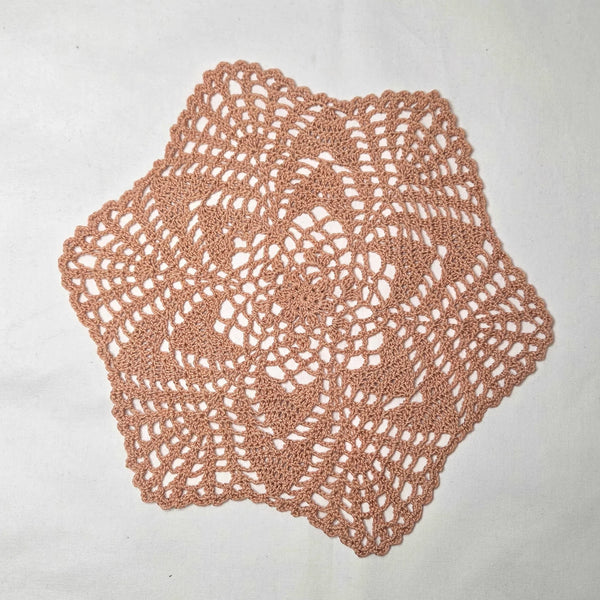 Handmade crochet doily in soft peach, featuring intricate lace pattern and scalloped edges for cozy home decor.