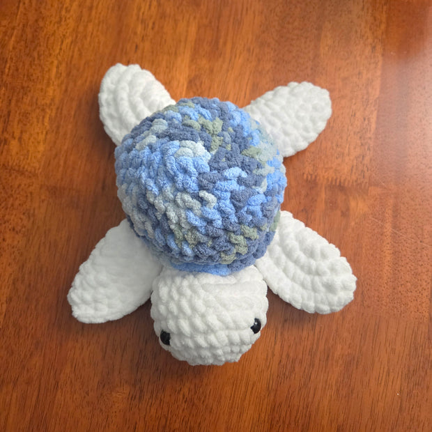 Handmade crochet turtle with blue shell and white limbs on wooden surface