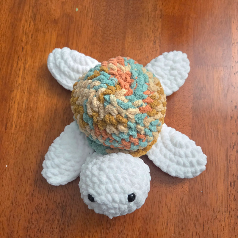 Handmade crochet turtle with colorful shell and white limbs on wooden surface