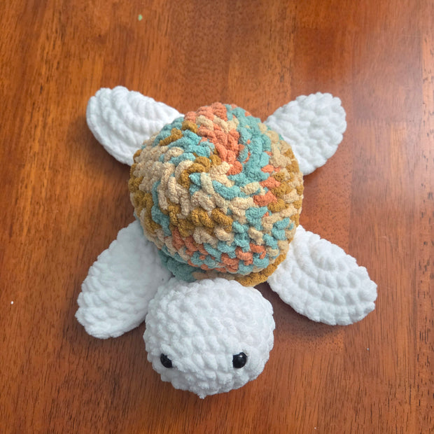 Handmade crochet turtle with colorful shell and white limbs on wooden surface
