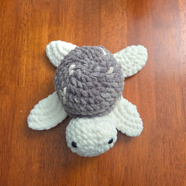 Handmade crochet turtle with gray shell and white limbs on wooden surface