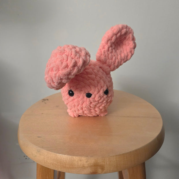 Pink crochet bunny with floppy ears on wooden stool, handmade cozy decor