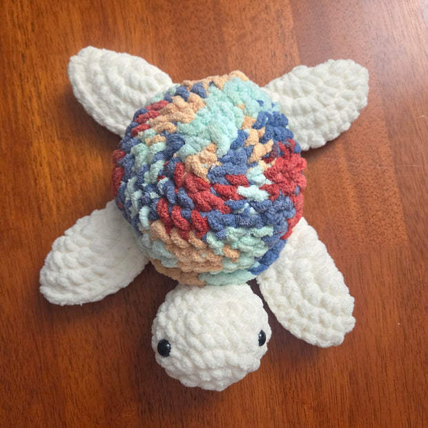 Handmade crochet turtle with colorful shell and white limbs on wooden surface