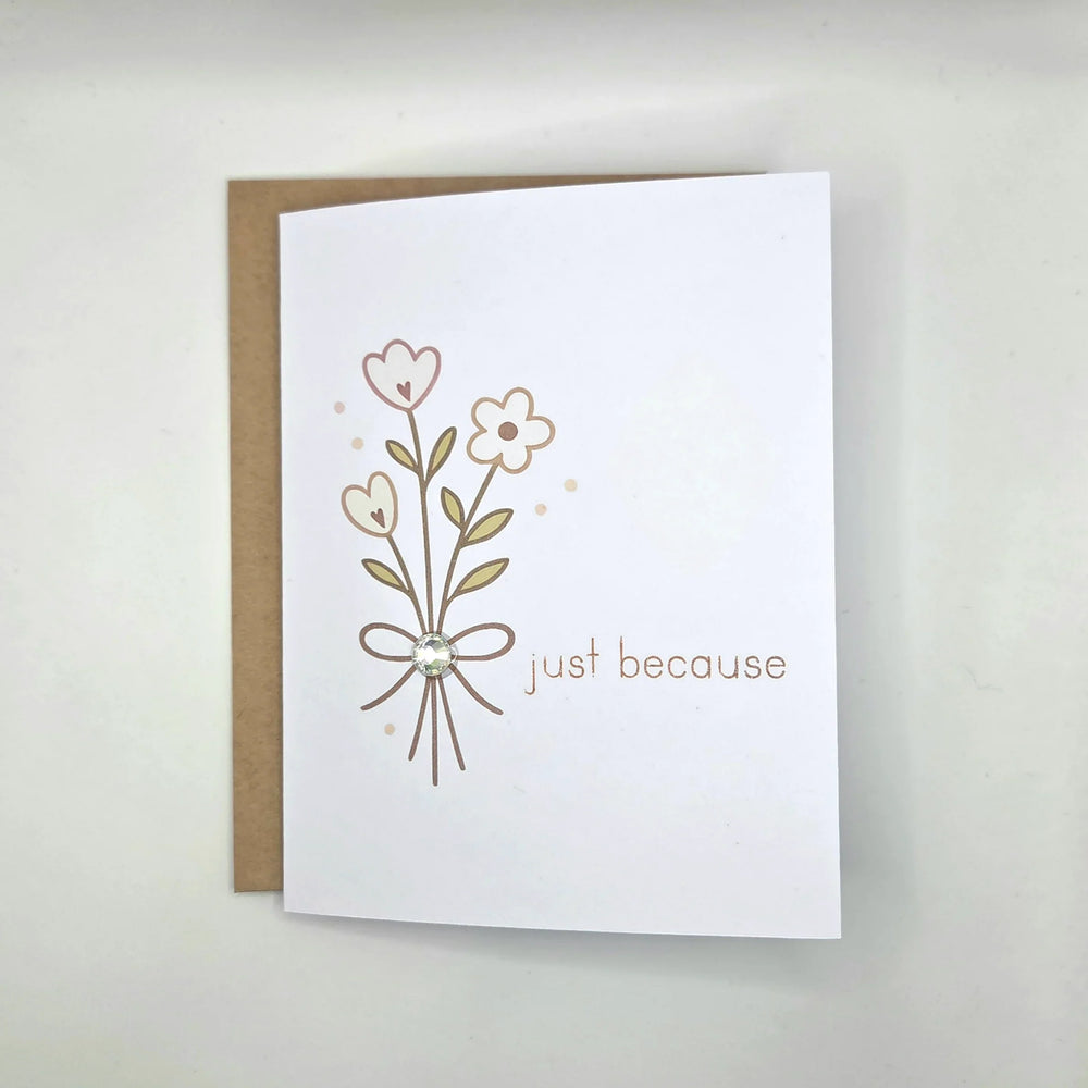 White greeting card with floral design, bow, gem, and 'just because' text, paired with kraft envelope
