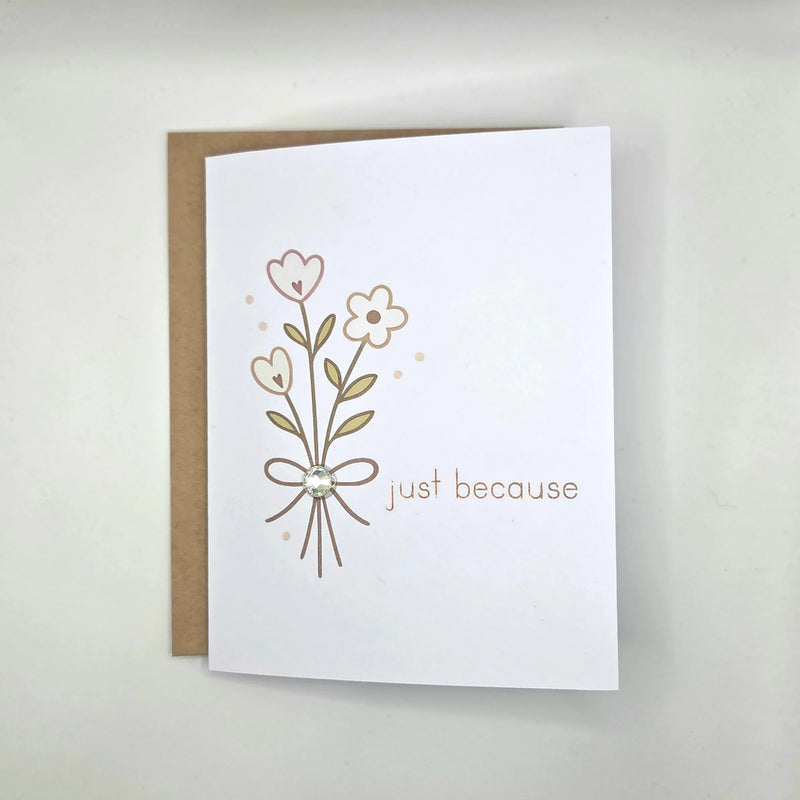 White greeting card with floral design, bow, gem, and 'just because' text, paired with kraft envelope