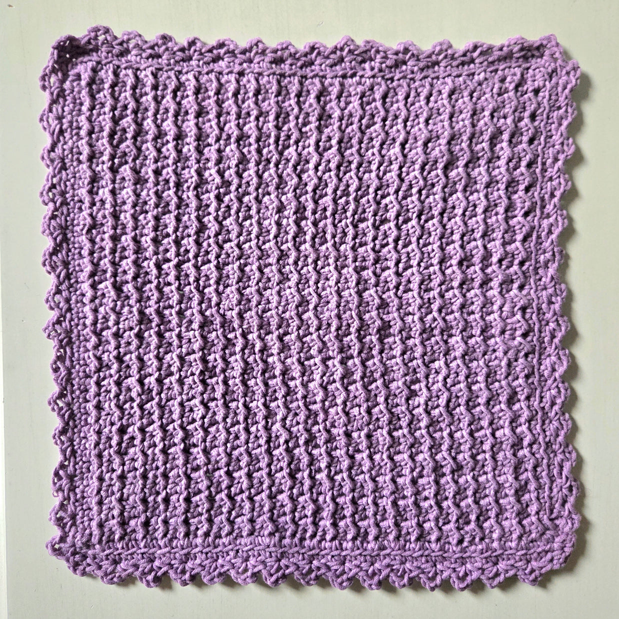 Handmade lavender crochet dishcloth with scalloped edges, perfect for cozy kitchen decor