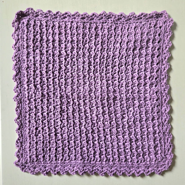 Handmade lavender crochet dishcloth with scalloped edges, perfect for cozy kitchen decor