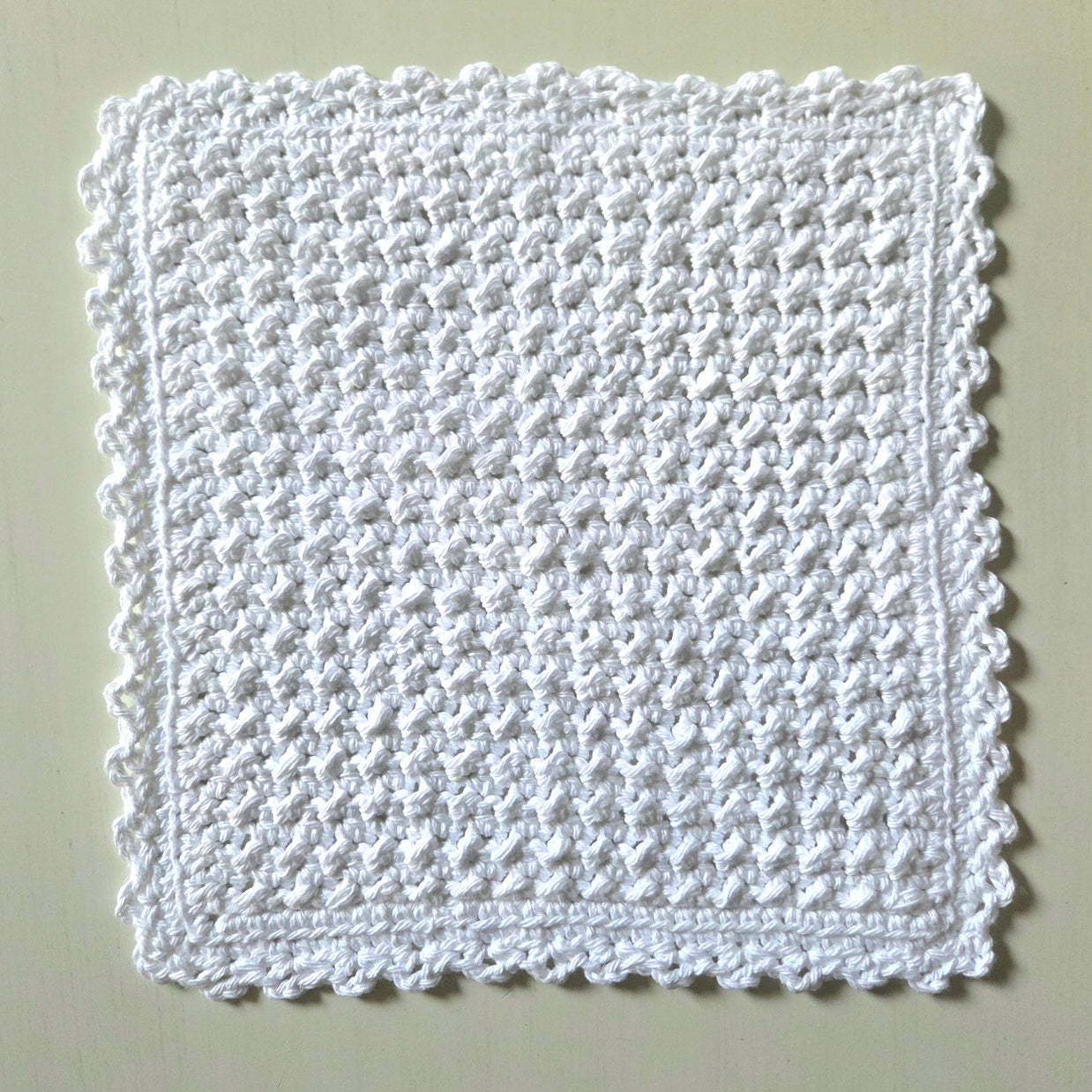 Handmade white crochet dishcloth with textured pattern and scalloped edges for cozy kitchen use