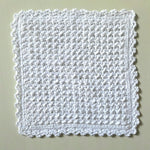 Handmade white crochet dishcloth with textured pattern and scalloped edges, perfect for cozy kitchen use.