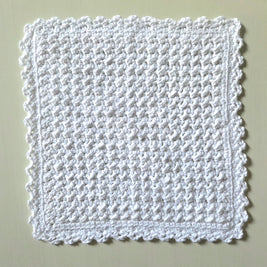 Handmade white crochet dishcloth with textured pattern and scalloped edges for cozy kitchen use