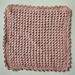 Handmade crochet dishcloth in soft pink with textured stitch pattern and scalloped edges