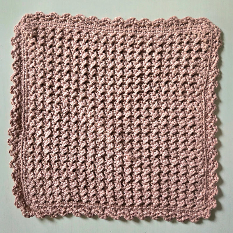 Handmade crochet dishcloth in soft pink with scalloped edges, perfect for cozy kitchen decor