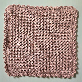 Handmade crochet dishcloth in soft pink with scalloped edges, perfect for cozy kitchen decor