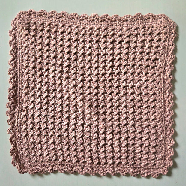 Handmade crochet dishcloth in soft pink with scalloped edges, perfect for cozy kitchen decor
