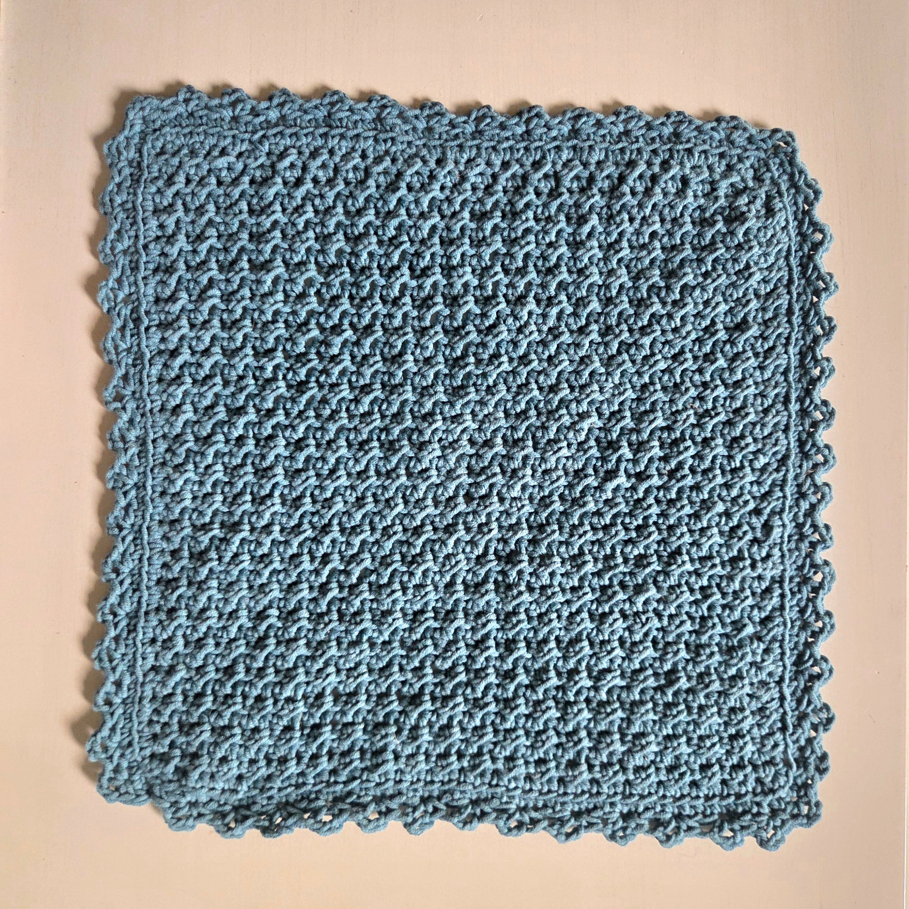 Handmade blue crochet dishcloth with scalloped edges, cozy and textured for kitchen use