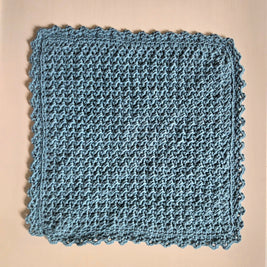 Handmade blue crochet dishcloth with scalloped edges, cozy and textured for kitchen use