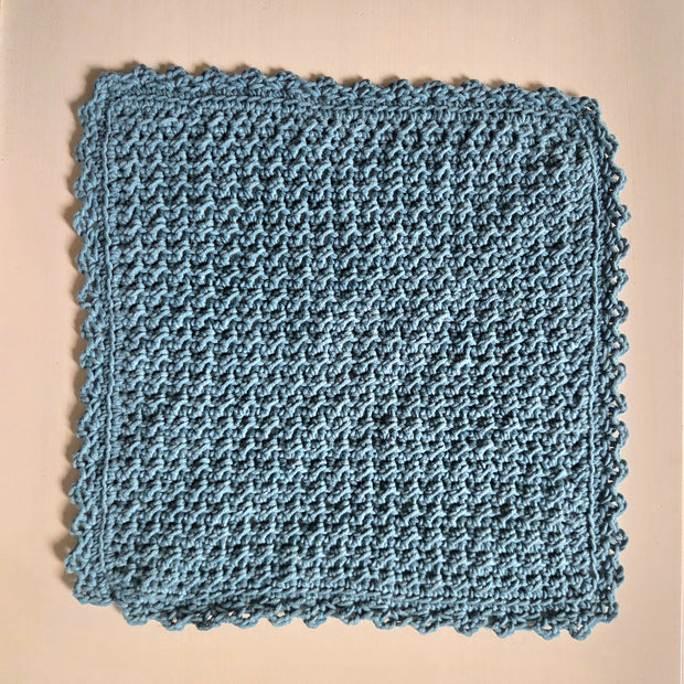 Handmade blue crochet dishcloth with scalloped edges, cozy and textured for kitchen use