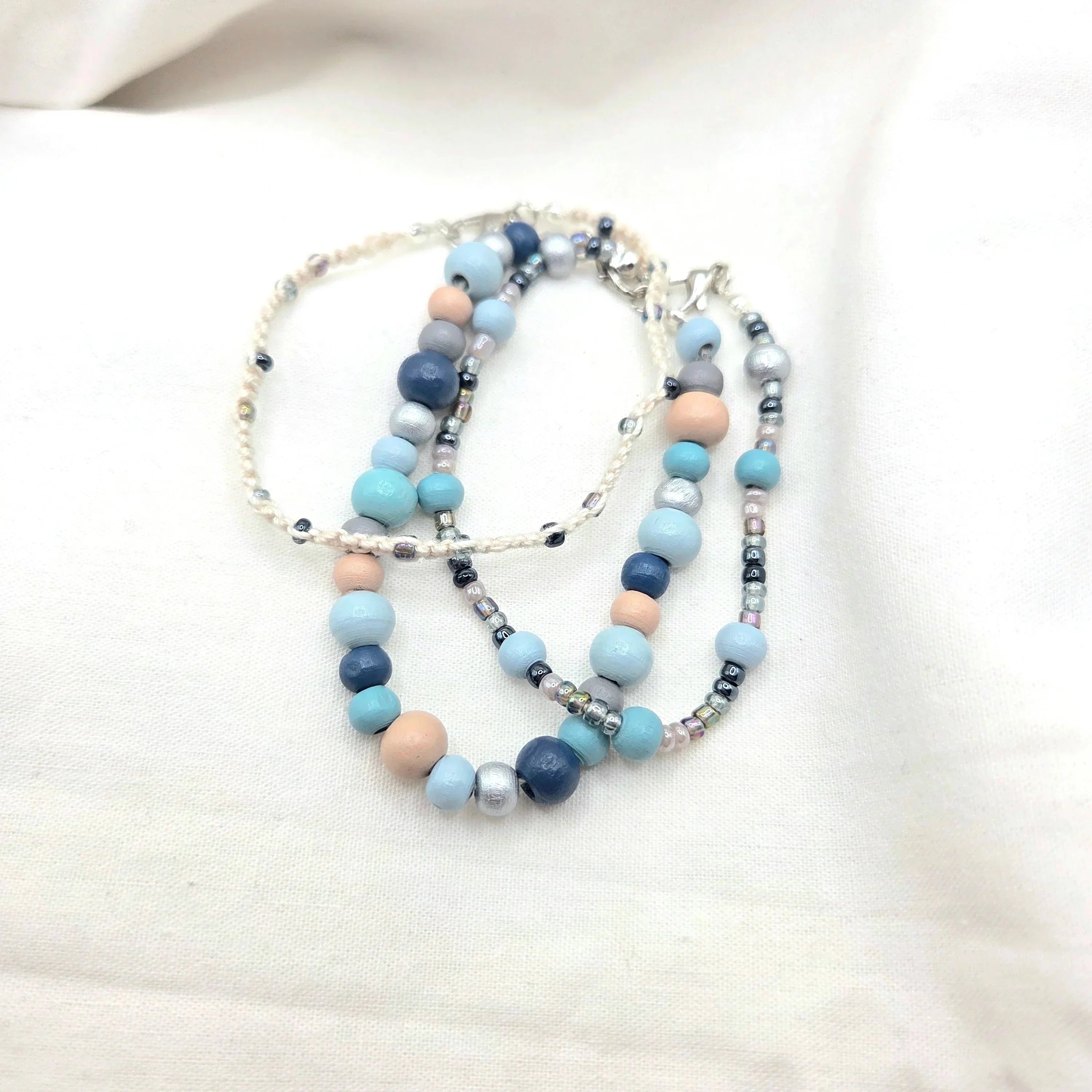 Handmade beaded necklace with blue, gray, and peach beads on cream cord, cozy artisan jewelry