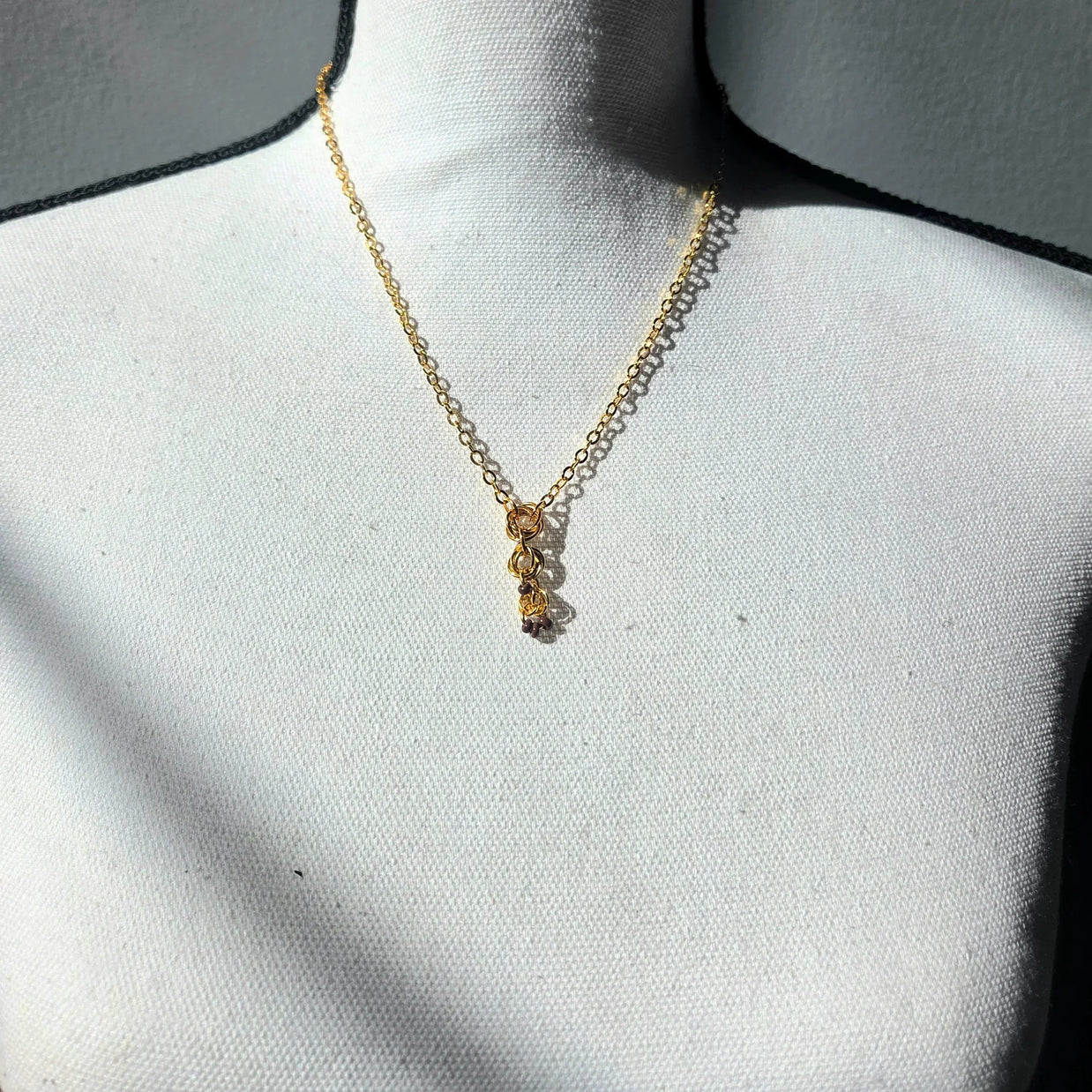 Delicate gold chain necklace with layered rings and tiny beads, displayed on white fabric bust.
