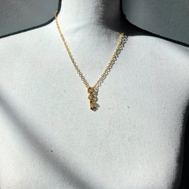 Delicate gold chain necklace with layered rings and tiny beads, displayed on white fabric bust.