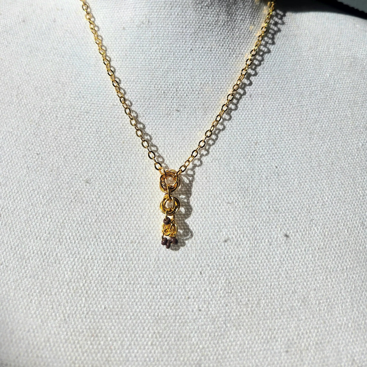 Gold chain necklace with interlocking rings and small beads, displayed on white fabric background