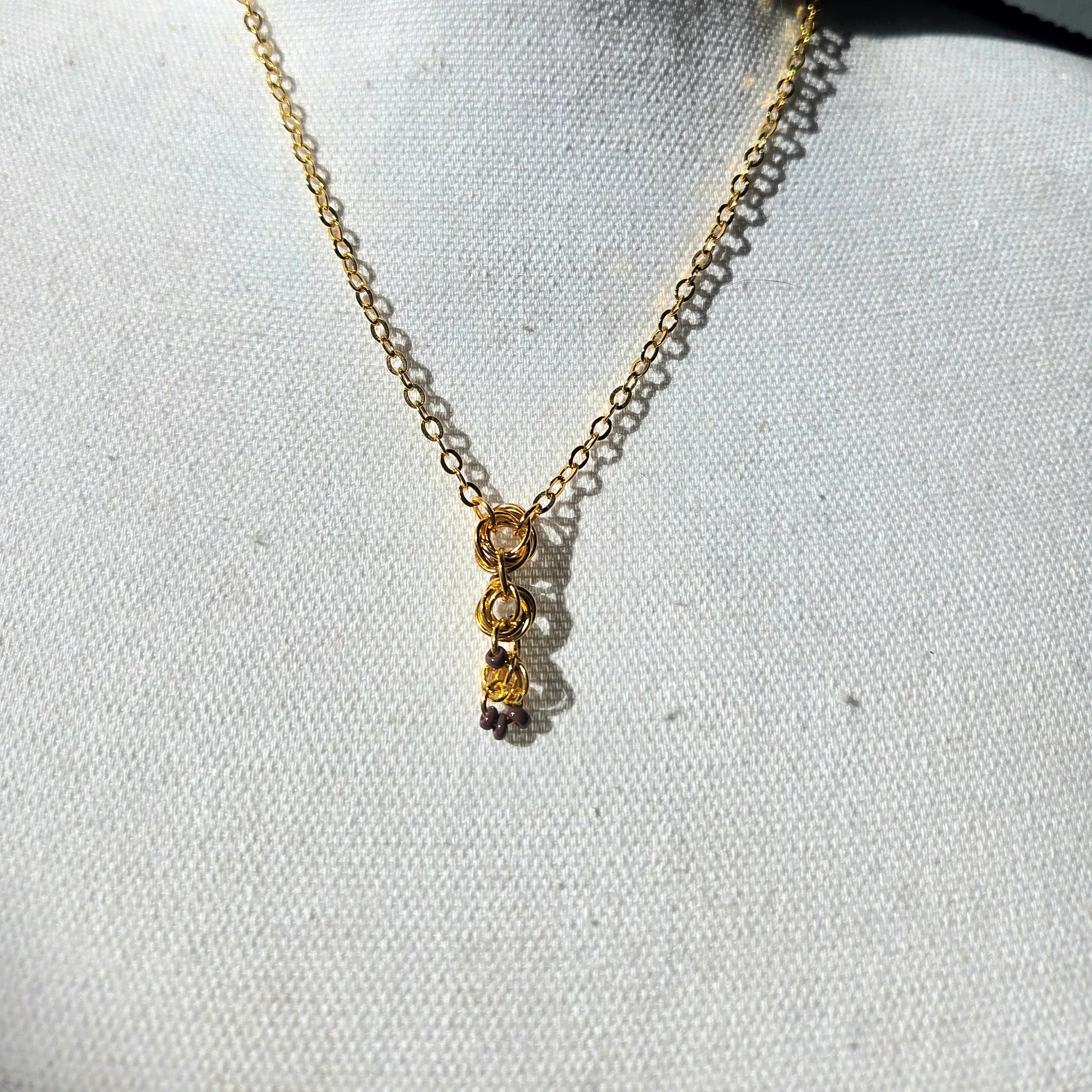 Gold chain necklace with interlocking rings and small beads, displayed on white fabric background