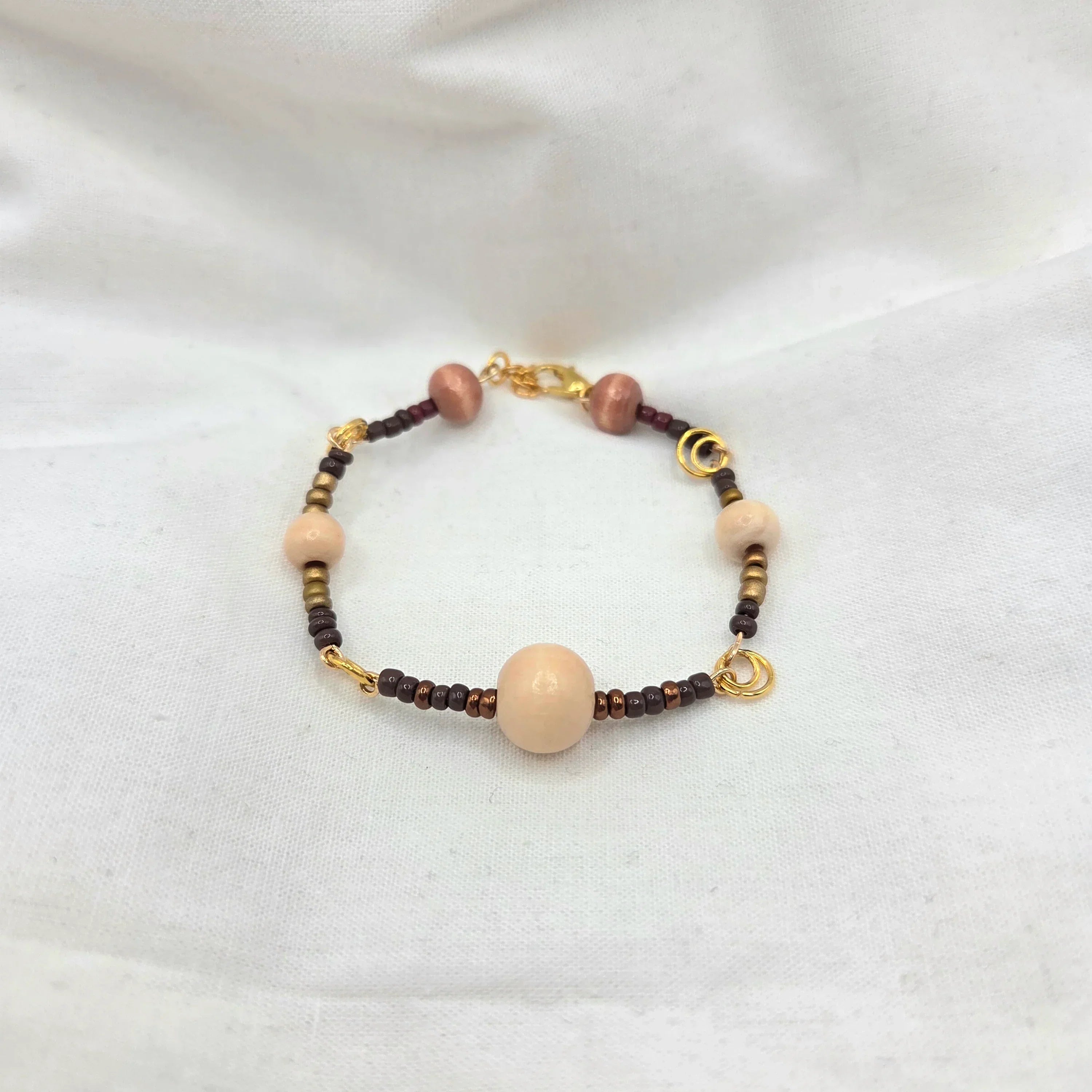 Handmade beaded bracelet with cream, brown, and gold beads on white fabric background