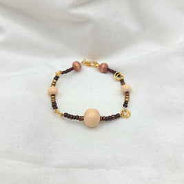 Handmade beaded bracelet with cream, brown, and gold beads on white fabric background