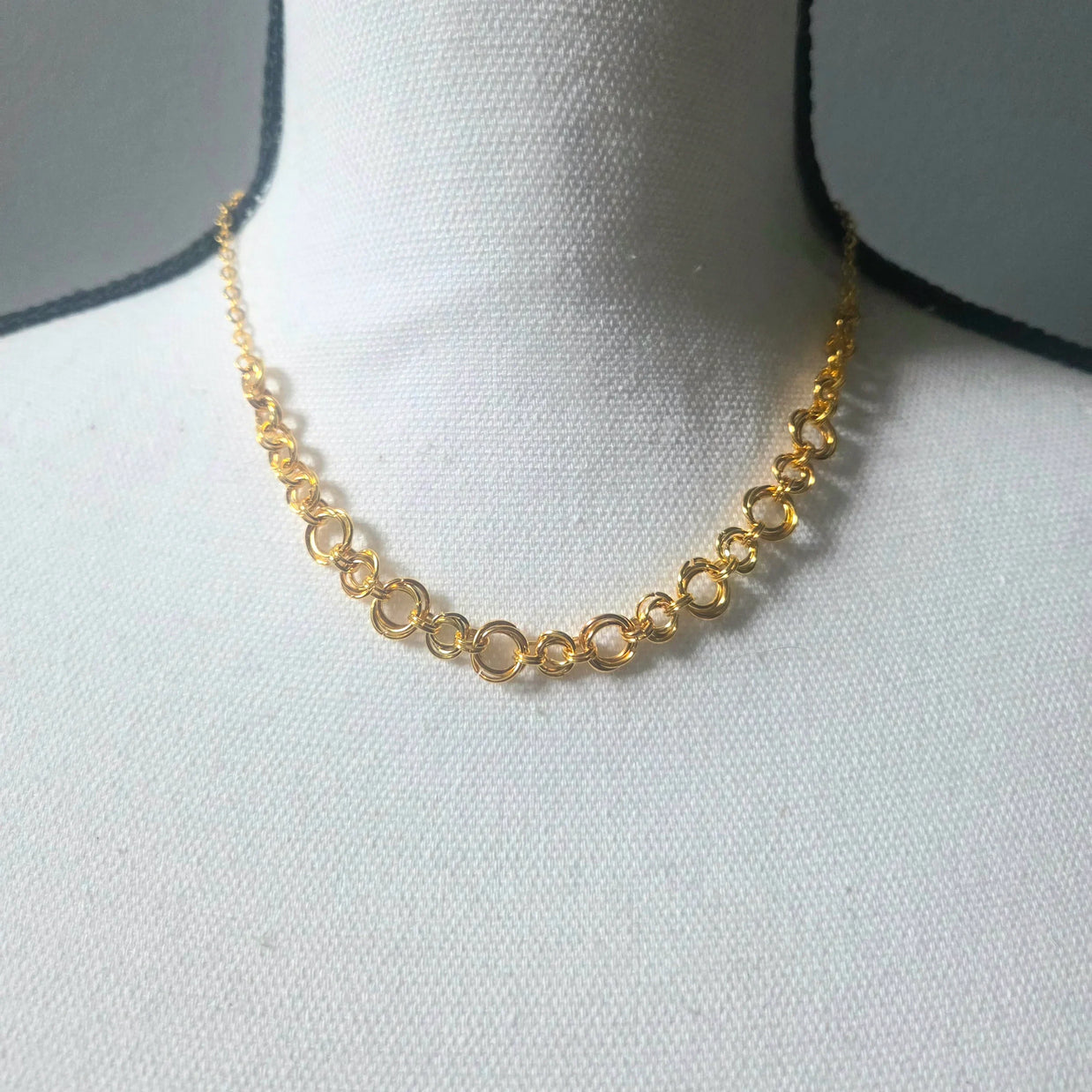 Gold chain necklace with interlocking rings displayed on white mannequin bust