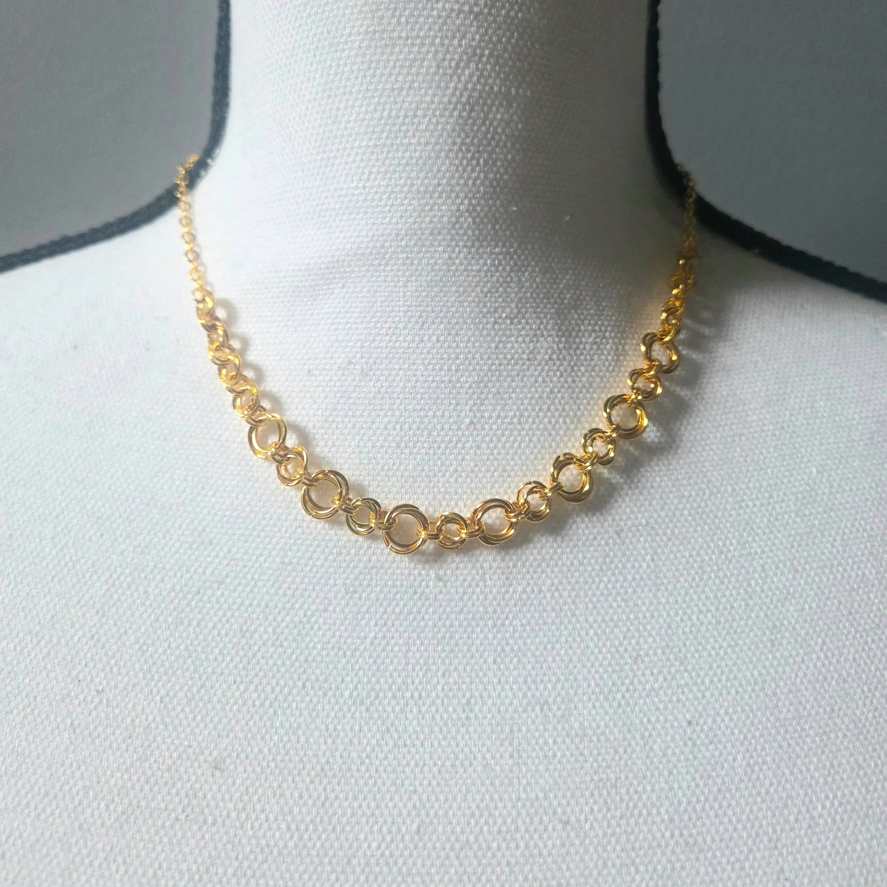 Gold chain necklace with interlocking rings displayed on white mannequin bust