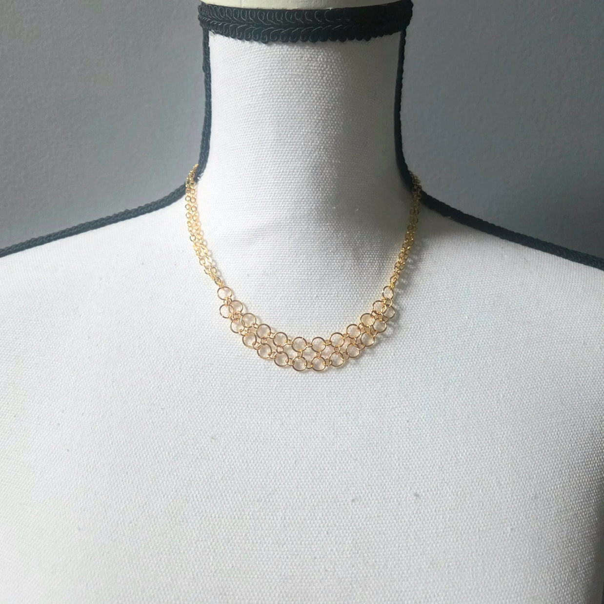 Delicate gold chainmaille necklace with interlocking rings, displayed on a mannequin for handmade jewelry lovers.