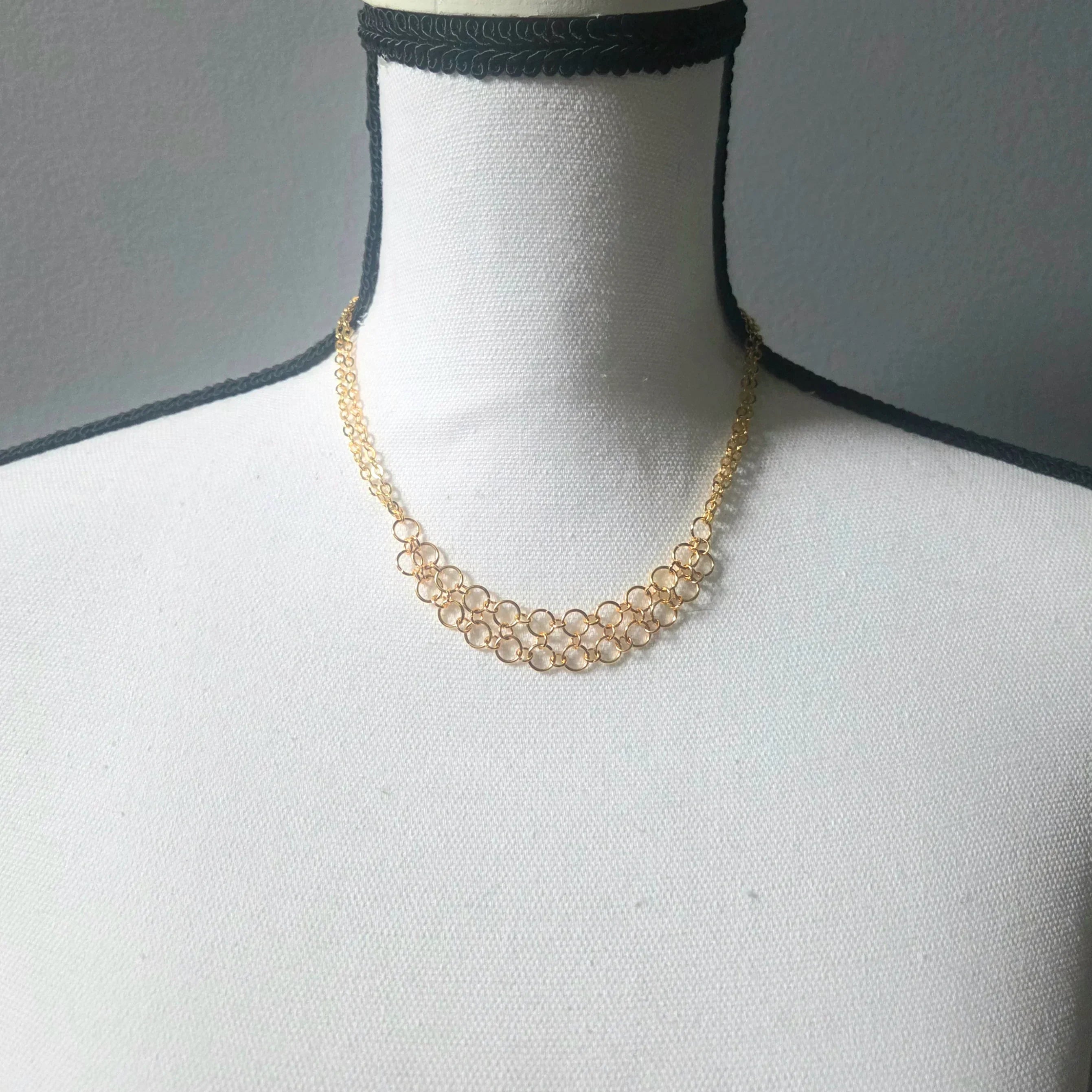 Delicate gold chainmaille necklace with interlocking rings, displayed on a mannequin for handmade jewelry lovers.