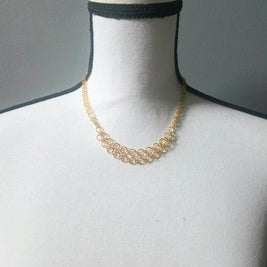Delicate gold chainmaille necklace with interlocking rings, displayed on a mannequin for handmade jewelry lovers.
