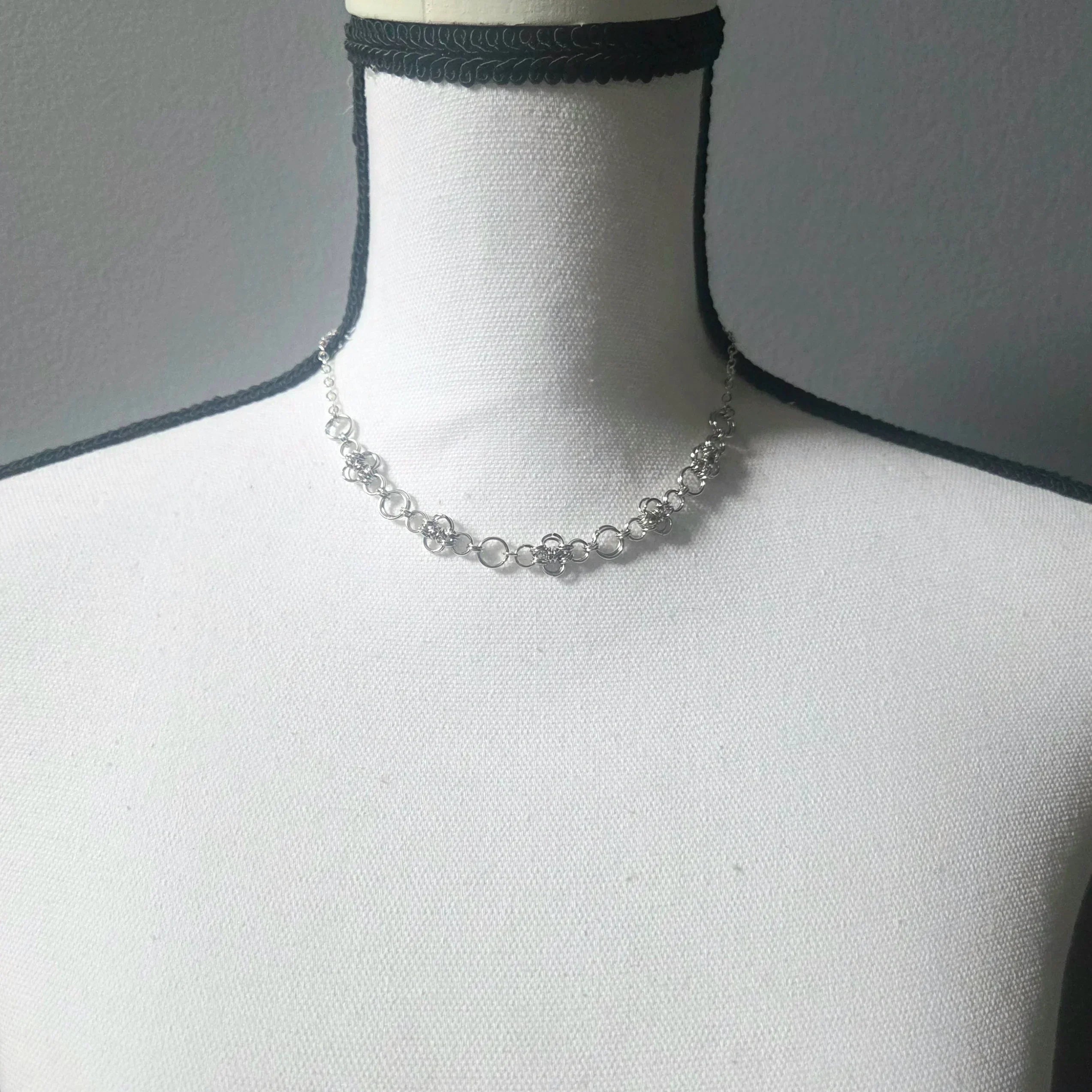 Delicate silver chainmaille necklace with floral links, displayed on a mannequin for handmade jewelry lovers.
