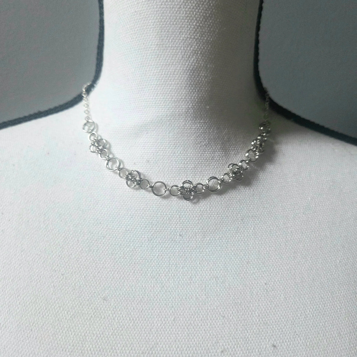 Silver chainmaille necklace with floral links on white display bust