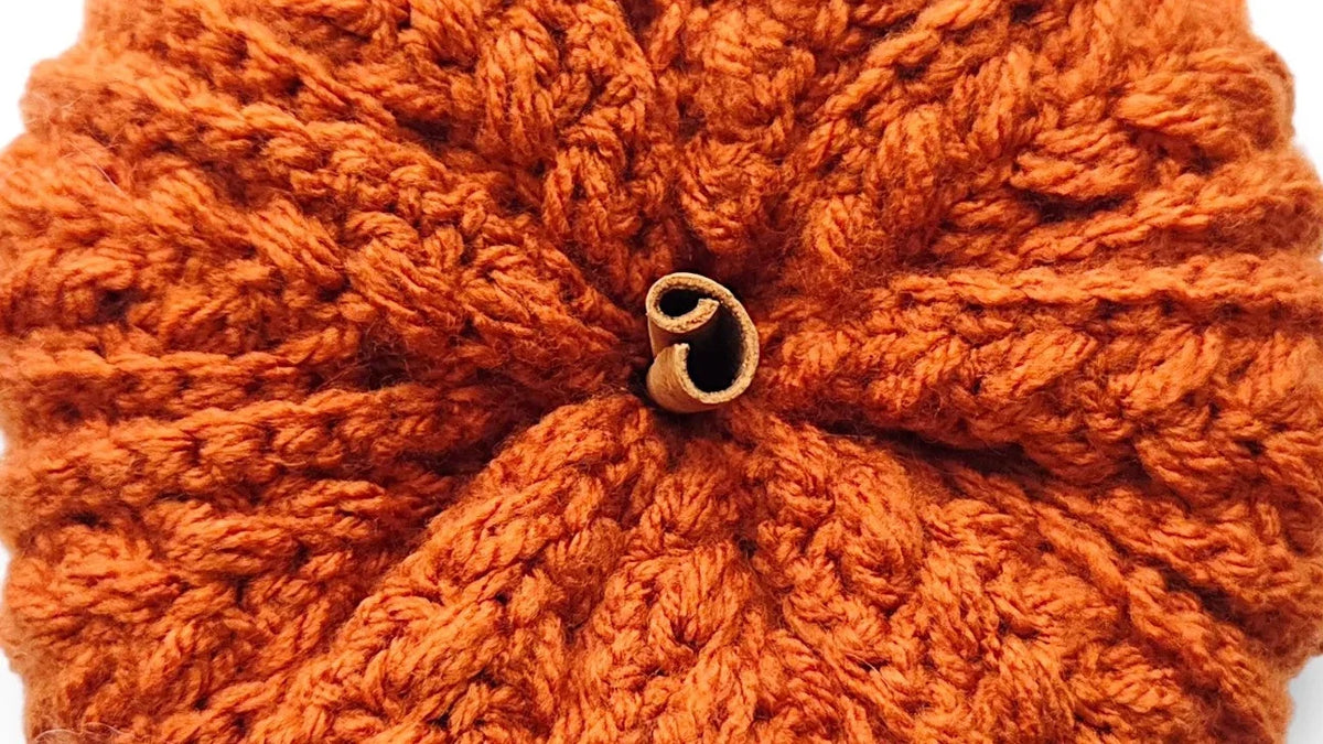 An orange crocheted pumpkin-shaped accessory with a small gold metal clasp at the top, shown on a clean white background.