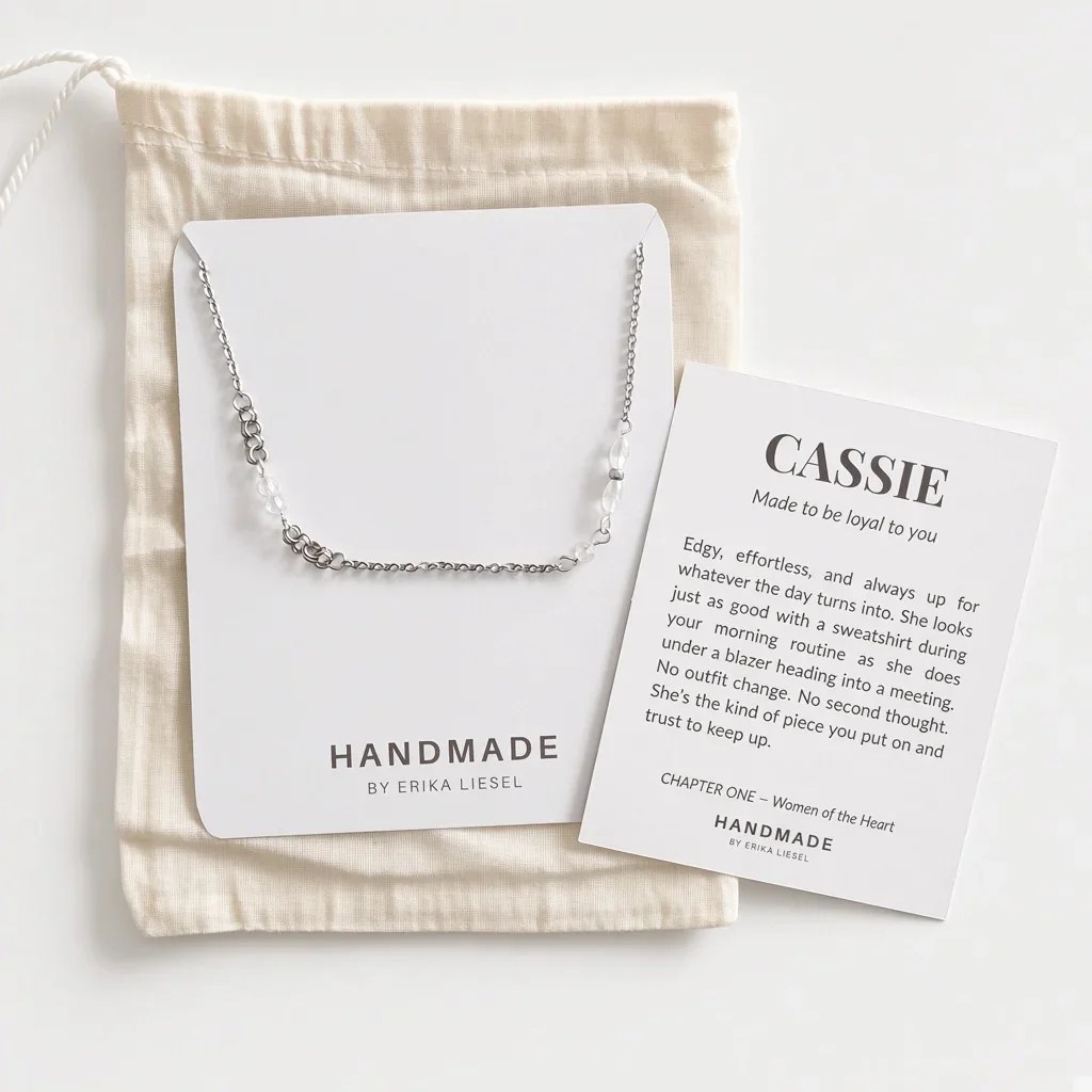 A silver chain necklace with a small heart pendant is displayed on a white card from HANDMADE BY ERIKA LIESEL, placed on top of a cream cotton drawstring pouch. A matching printed card with the name 'CASSIE' and a short poem is also visible on a clean white background.